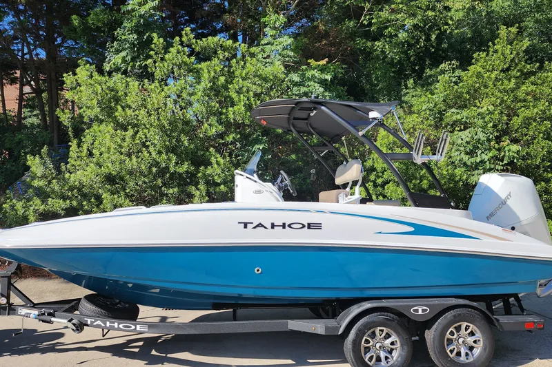 The Image of 2026 Tahoe 2150 CC boat on trailer, blue and white design, surrounded by greenery. - 1