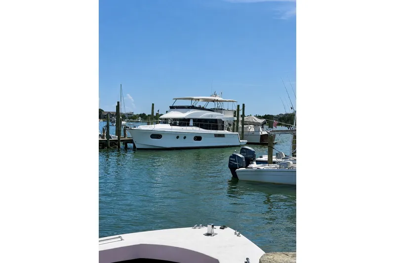 Slide: The Image of 2025 Beneteau Swift Trawler 48 docked in a serene marina setting. - 2