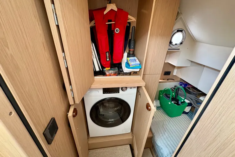 Slide: The Image of Laundry area inside 2025 Beneteau Swift Trawler 48, featuring a washing machine and storage space. - 10