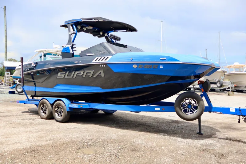Slide: The Image of 2022 Supra SE 450 boat on trailer, blue and black design, parked outdoors. - 6