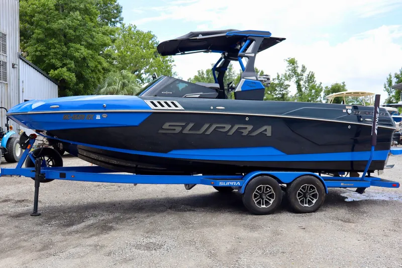 Slide: The Image of 2022 Supra SE 450 boat in blue and black on a trailer, parked outdoors. - 1