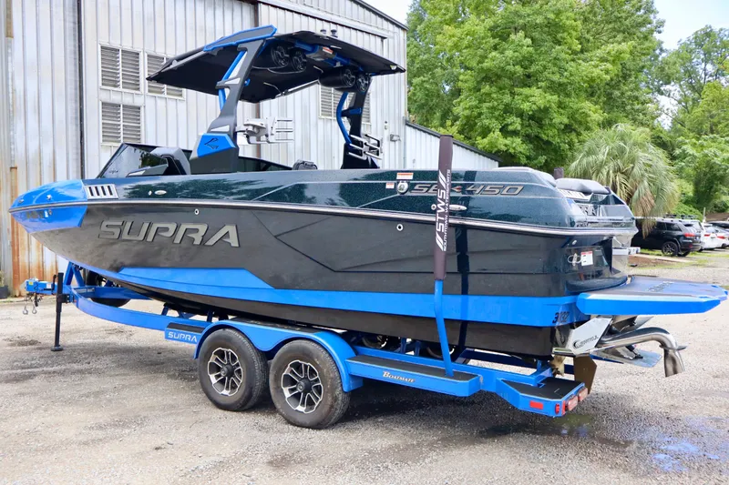 Slide: The Image of 2022 Supra SE 450 boat on trailer, blue and black design, parked outdoors. - 2