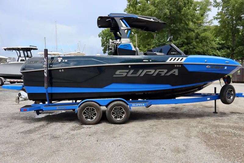 Slide: The Image of 2022 Supra SE 450 boat on trailer, blue and black design, parked outdoors. - 5