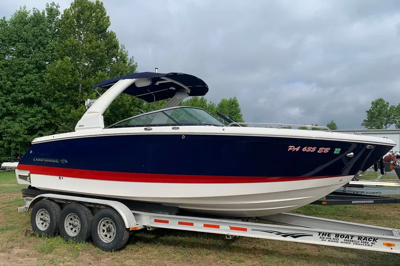 The Image of 2022 Chaparral 28 Surf boat on trailer, blue and white with red stripe, parked outdoors. - 0