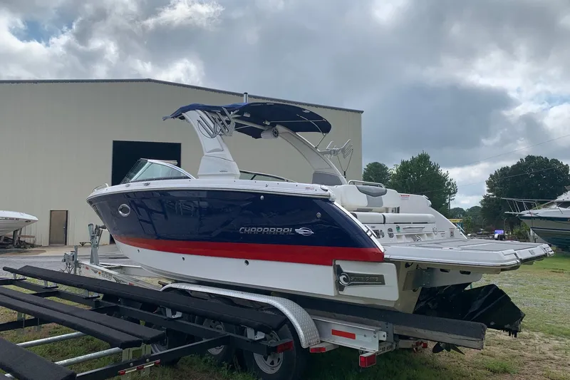 Slide: The Image of 2022 Chaparral 28 Surf boat on trailer, parked outdoors near a large building. - 1