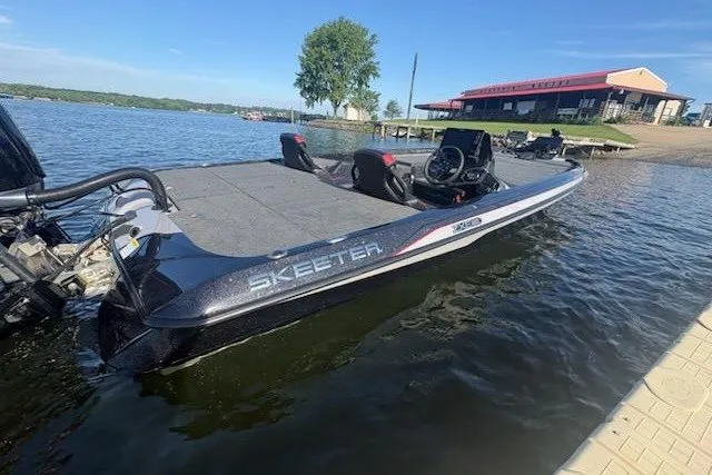 The Image of 2026 Skeeter ZXE20 boat docked on a sunny lake with a red-roofed building nearby. - 5