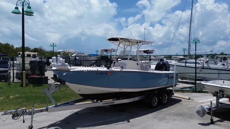 Slide: The Image of 2024 Mako 214CC on a trailer at a marina, surrounded by other boats and a fence. - 22