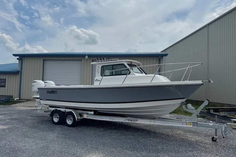 The Image of 2027 Parker 247 Explorer boat on trailer, parked outside a warehouse under a cloudy sky. - 0