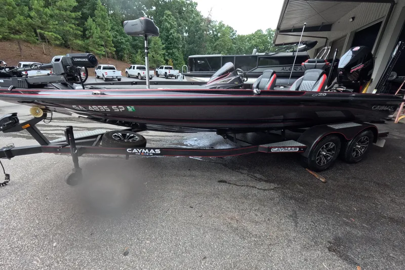 The Image of 2021 Caymas boat on trailer, parked outdoors, surrounded by trees and vehicles. - 1