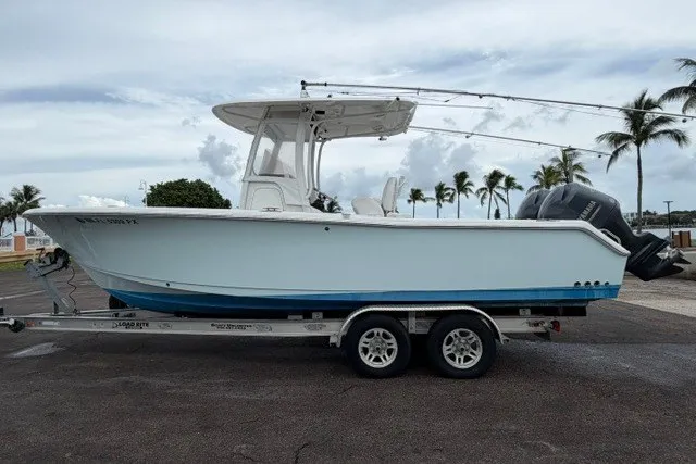 Slide: The Image of 2014 Sea Hunt Gamefish 25 boat on trailer, parked near palm trees under cloudy sky. - 6