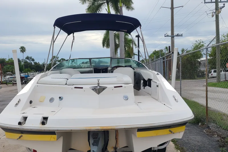 Slide: The Image of 2005 Regal 2200 Bowrider boat with canopy, parked near palm trees and fencing. - 19