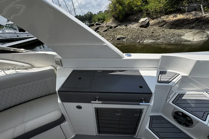 Slide: The Image of 2021 Sea Ray SLX 350 Outboard interior with seating and storage, docked near rocky shoreline. - 9