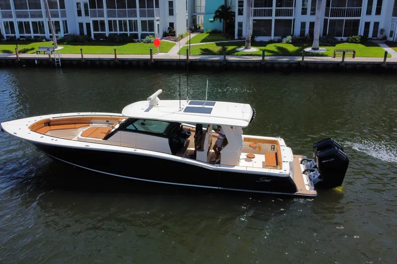 Slide: The Image of 2021 Scout 425 LXF boat cruising on a calm waterway near waterfront homes. - 13