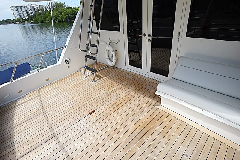 Slide: The Image of 1996 Hatteras yacht deck with wooden flooring, seating, and ladder near calm waters. - 29