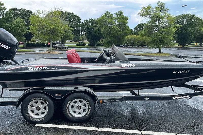 Slide: The Image of 2008 Triton Tr-196 SC boat on trailer in parking lot, surrounded by trees. - 0