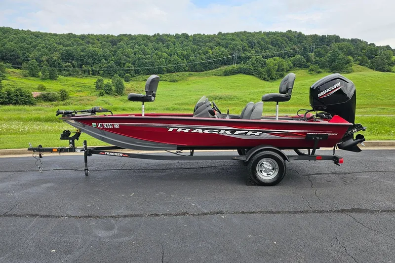 The Image of 2024 Tracker Pro Team 175 TXW boat on trailer, parked on asphalt with green hills in background. - 0