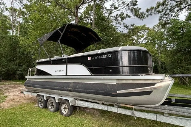 Slide: The Image of 2023 Crest Classic DLX 220 pontoon boat on trailer, surrounded by trees. - 4