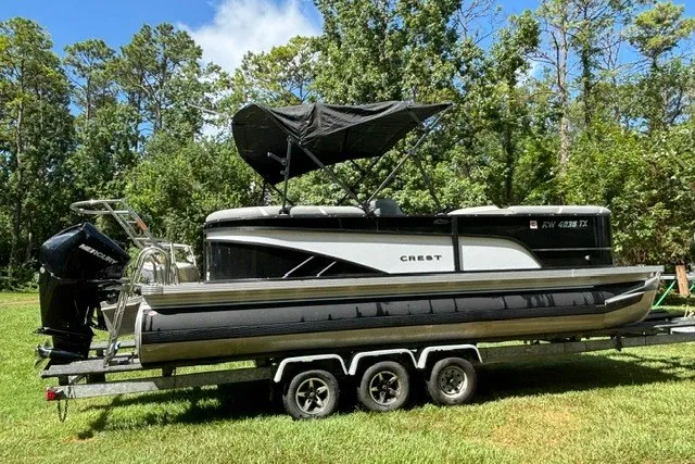 Slide: The Image of 2023 Crest Classic DLX 220 pontoon boat on trailer, parked on grass with trees in background. - 20