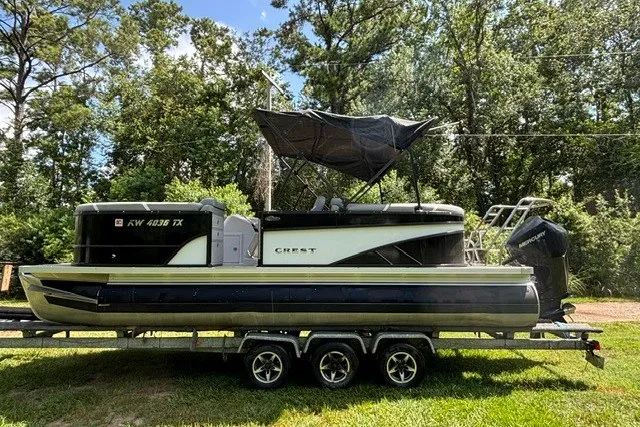Slide: The Image of 2023 Crest Classic DLX 220 pontoon boat on trailer, surrounded by lush greenery. - 17