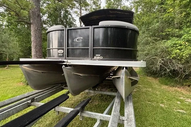 Slide: The Image of 2023 Crest Classic DLX 220 pontoon boat on trailer, surrounded by lush greenery. - 5