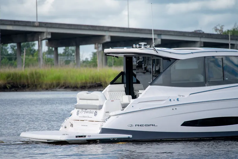 Slide: The Image of 2025 Regal 36 Grande Coupe yacht cruising on a serene waterway under a bridge. - 2