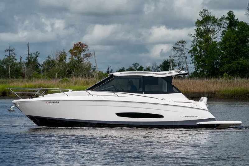 Slide: The Image of 2025 Regal 36 Grande Coupe cruising on a serene lake with lush greenery. - 7