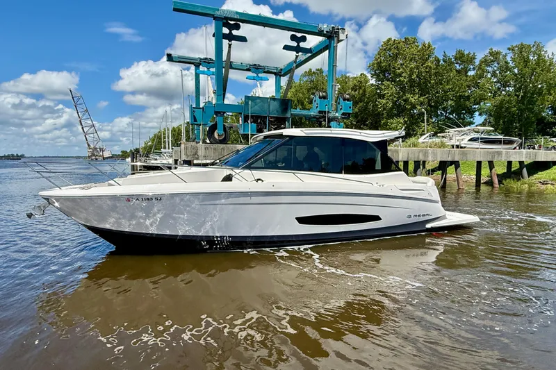 The Image of 2025 Regal 36 Grande Coupe yacht on water, with marina backdrop and blue sky. - 0
