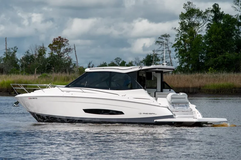 Slide: The Image of 2025 Regal 36 Grande Coupe cruising on a serene river with lush greenery. - 6