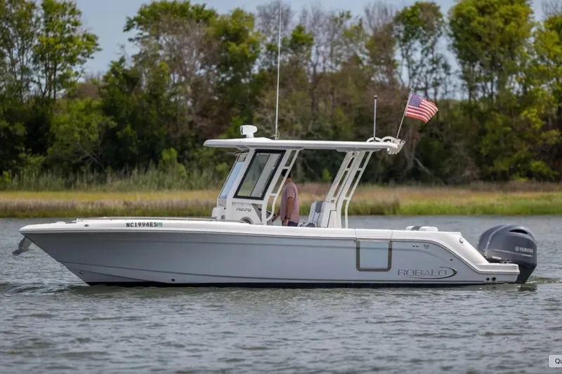Slide: The Image of 2021 Robalo R272 Center Console boat on water, American flag, lush greenery background. - 3
