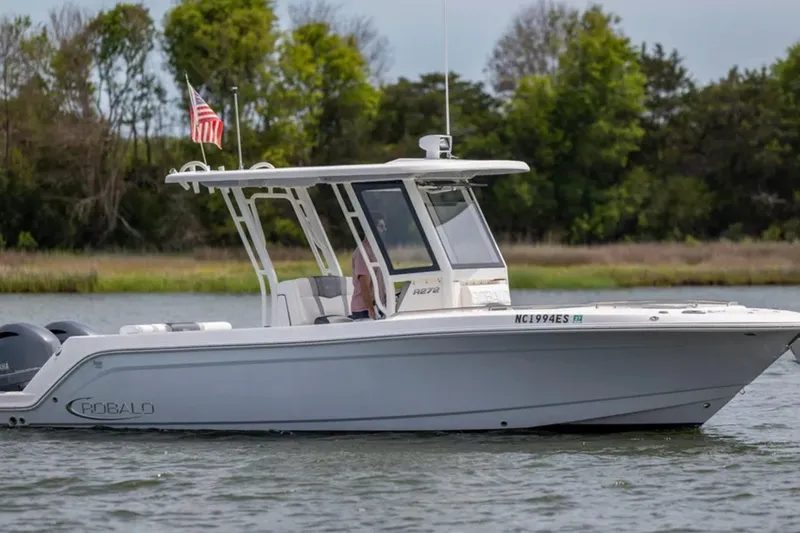 Slide: The Image of 2021 Robalo R272 Center Console boat cruising on a calm lake with trees in the background. - 2