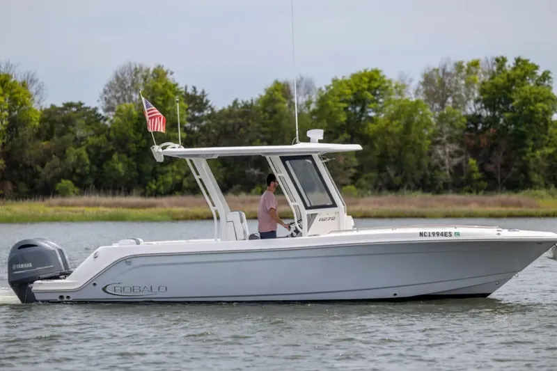 The Image of 2021 Robalo R272 Center Console boat cruising on a calm lake with trees in the background. - 0