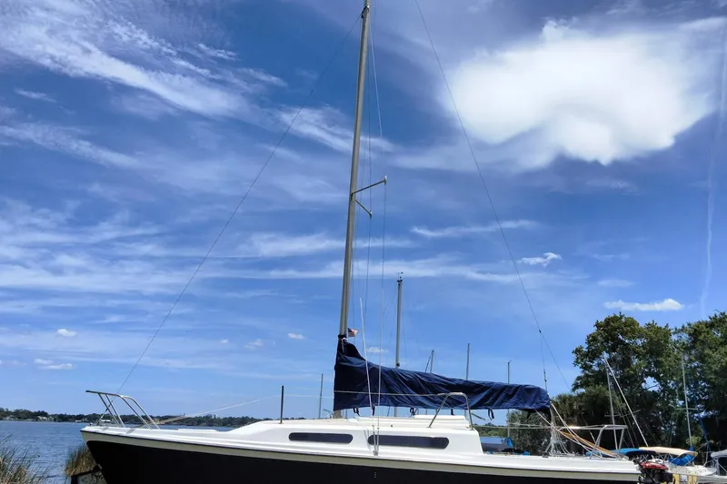 The Image of 1980 MacGregor 25 sailboat docked under a clear blue sky with scattered clouds. - 5