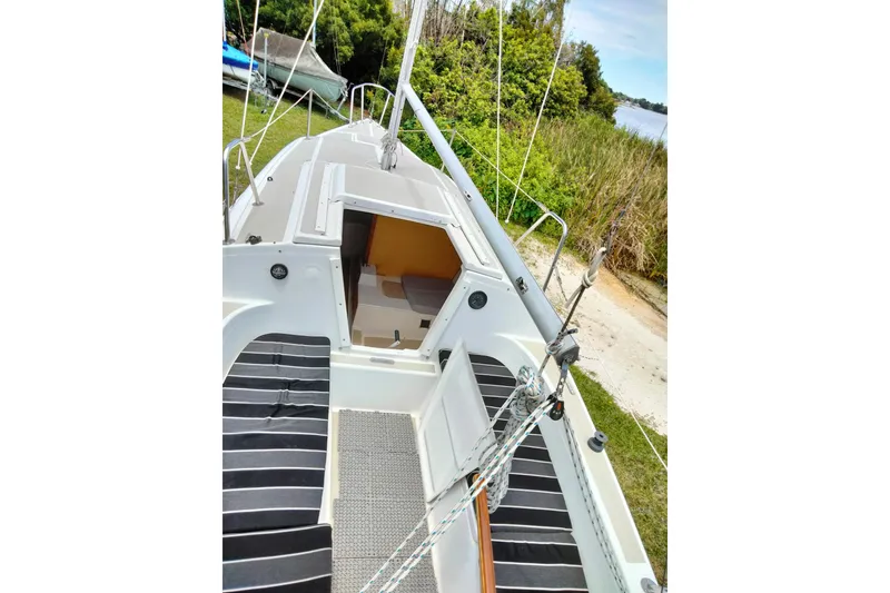 Slide: The Image of 1980 MacGregor 25 sailboat deck with open cabin, surrounded by lush greenery. - 13