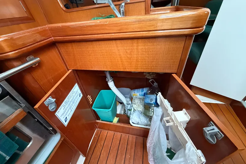 Slide: The Image of Under-sink storage on a 2001 Beneteau 331 sailboat, featuring wooden cabinetry and cleaning supplies. - 25