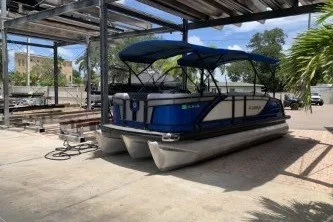 The Image of 2021 Godfrey Monaco 235 SFL pontoon boat parked under a canopy in a sunny outdoor setting. - 1