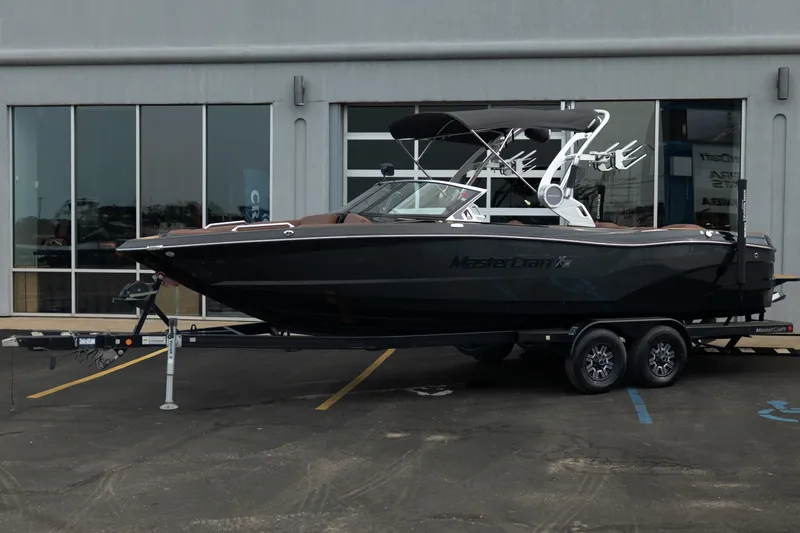 Slide: The Image of 2020 MasterCraft XT25 boat on trailer, parked outside a building. - 2