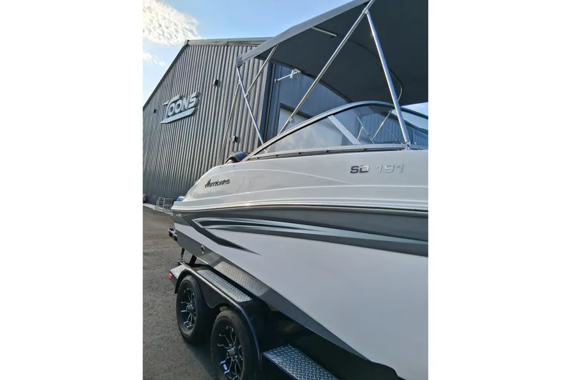 Slide: The Image of 2024 Hurricane SunDeck 191 OB boat on trailer, parked near a metal building. - 8