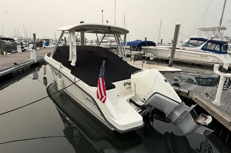 Slide: The Image of 2022 Boston Whaler 240 Vantage docked, covered, with American flag, in marina setting. - 61