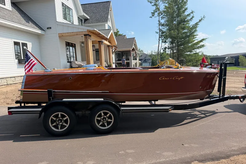 Slide: The Image of 1953 Chris Craft Riviera boat on trailer, parked near a house, with American flag displayed. - 6
