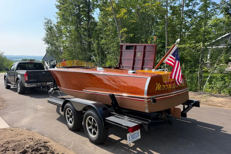 Slide: The Image of 1953 Chris Craft Riviera boat on trailer, towed by a truck, surrounded by trees. - 30
