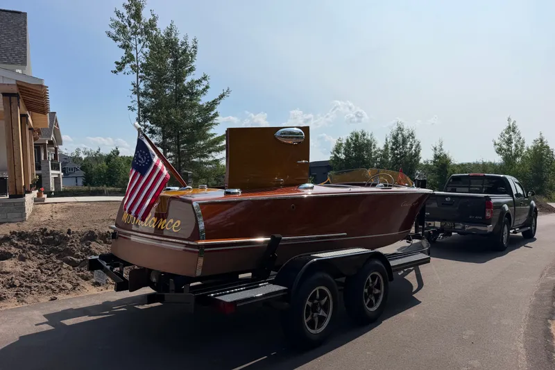Slide: The Image of 1953 Chris Craft Riviera boat on trailer, American flag, parked near house and trees. - 29