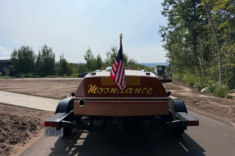 Slide: The Image of 1953 Chris Craft Riviera boat "Moondance" on trailer with American flag, surrounded by trees. - 4