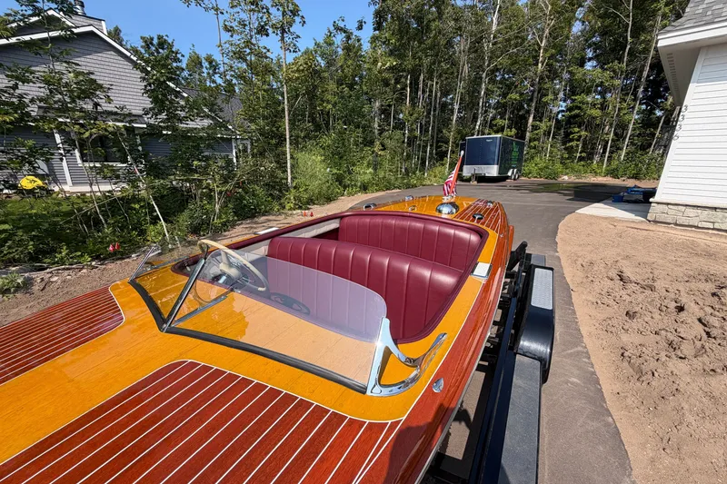 Slide: The Image of 1953 Chris Craft Riviera boat with polished wood finish and red interior, parked outdoors. - 11