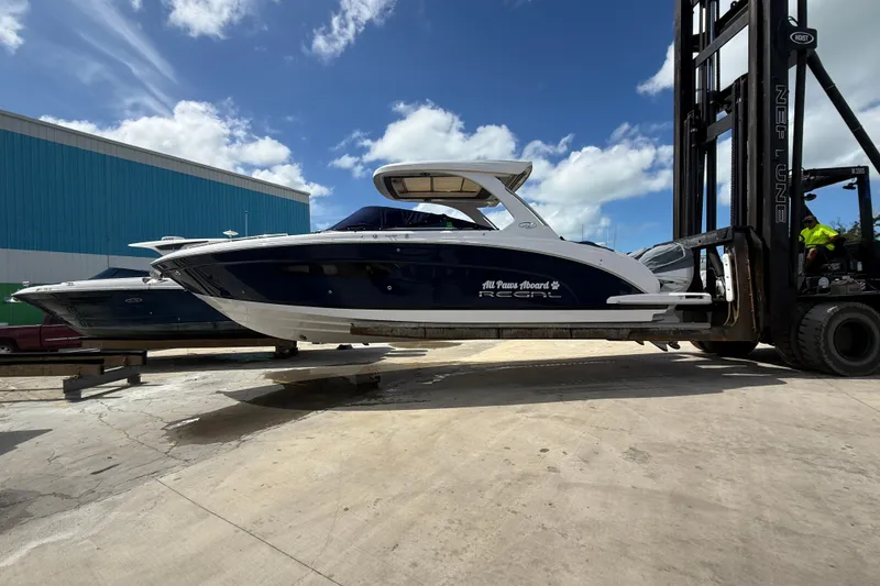 Slide: The Image of 2022 Regal 33 OBX boat lifted by forklift under a clear blue sky. - 2