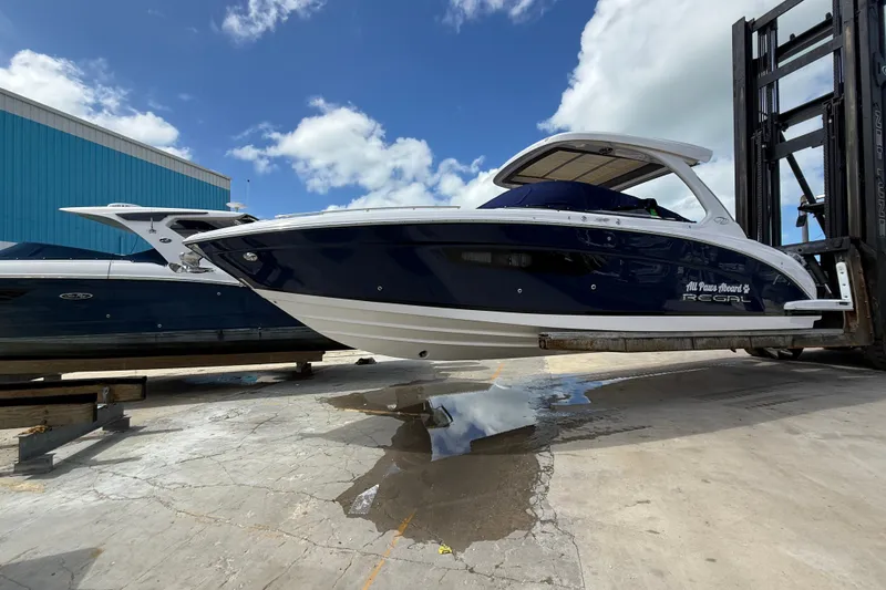 Slide: The Image of 2022 Regal 33 OBX boat lifted on a forklift, blue and white design, clear sky background. - 1