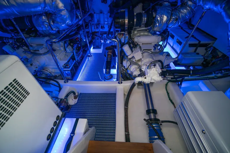 Slide: The Image of The engine room of a 2013 Ocean Alexander 65 Pilothouse with blue lighting and complex piping. - 55