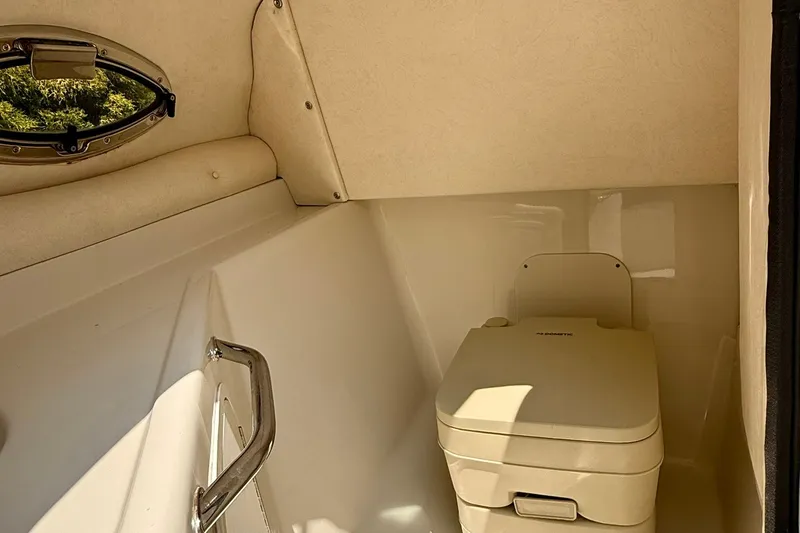 Slide: The Image of 2005 Sea Ray 270 Sundeck interior with compact marine toilet and porthole window. - 11