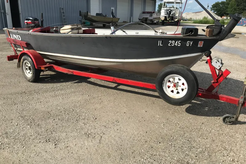 Slide: The Image of 1989 Lund 16 Pike SS boat on red trailer, parked on gravel near industrial buildings. - 19