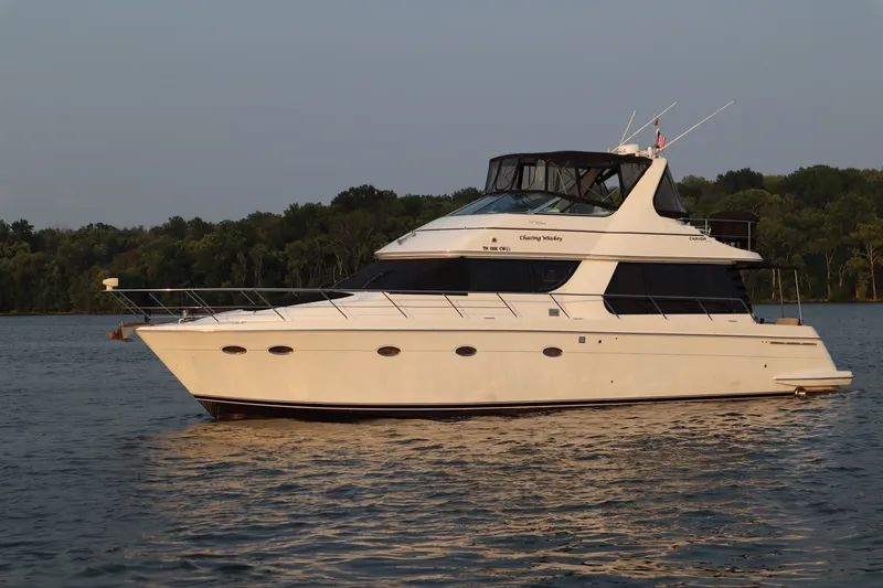 The Image of 1999 Carver Yacht Voyager 530 cruising on a serene lake with lush green shoreline. - 1