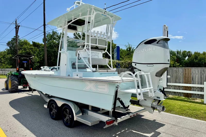 Slide: The Image of 2024 Shallow Sport 25 X3 boat with Suzuki engine on trailer, parked outdoors. - 2